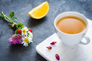 Green tea in cup with lemon and small bouquet of flowers on side