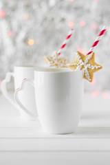 Gingerbread star put on a white cup with hot chocolate on the background of bokeh and snow. Selective focus