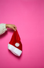 Womans hand holding a Santa Claus hut on pink background