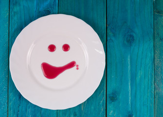 Smiling white plate with red syrup and blue wooden background
