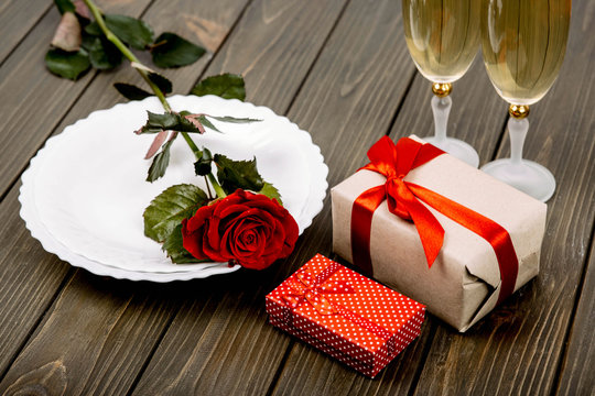 plate with red rose and gift boxes lie on wooden surface