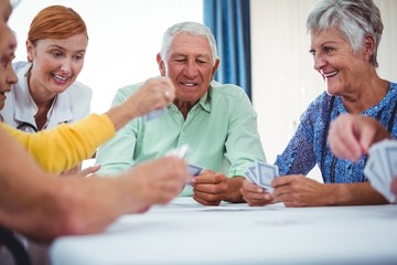 Smiling nurse and seniors people playing cards