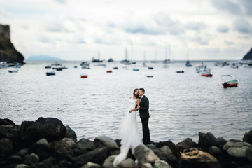 Tender wedding couple stands on the rocks before the bay with ya
