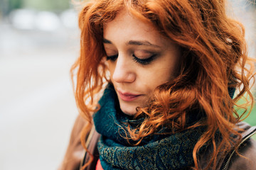 Portrait of young beautiful caucasian redhead woman posing outdoor in the city overlooking - serene, carefree, thoughtless concept