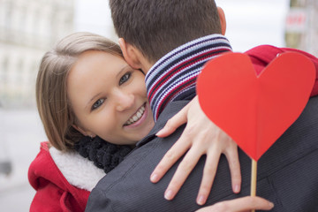 Young Couple in Love Hugging. Girlfriend Holding Red Heart and Smiling. Love and Valentines Day Concept.