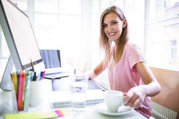 Female graphic designer having coffee at desk