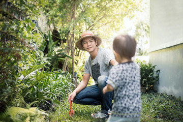 Naklejka na ściany i meble Happy joyful young father with his little daughter. Father and little kid having fun outdoors in backyard garden, playing together in home garden. Dad with his child laughing and enjoying nature.