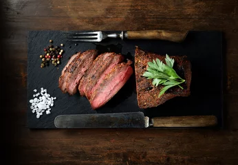 Papier Peint photo Steakhouse steak grillé sur ardoise noire, couteau et fourchette.