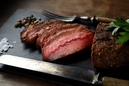 grilled steak on a black slate, knife and fork. 