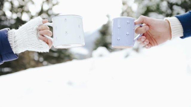 Man and woman hands in knitting mittens with cups of hot tea on winter forest gl