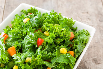 Kale salad in bowl with carrot, pepper and sweet corn on wooden background
