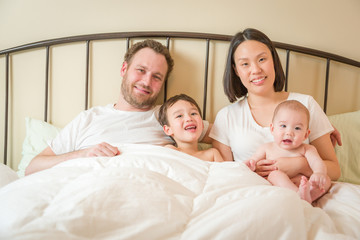 Fototapeta premium Young Mixed Race Chinese and Caucasian Baby Boys Laying In Bed with Their Father and Mother.