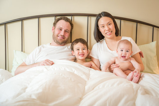 Young Mixed Race Chinese and Caucasian Baby Boys Laying In Bed with Their Father and Mother.