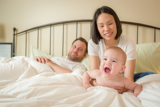 Young Mixed Race Chinese and Caucasian Baby Boy Laying In Bed with His Father and Mother.
