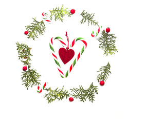 Christmas wreath made of green thuja twigs, red wild rose fruits, xmas tree decorations and candy canes on white background. Top view, flat lay. Copy space for text