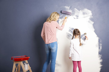 Shot of a woman and and her cute daughter painting the wall at home while renovation their home. 