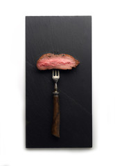 Slices of Medium rare grilled Steak Ribeye on meat fork on white background