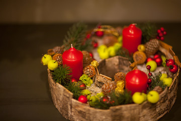 red Christmas candle in a basket with berries and fir cones with green apples