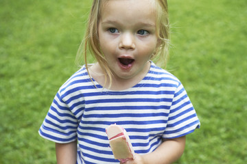 Fototapeta premium Beautiful little girl eats ice-cream in the summer with green grass background.