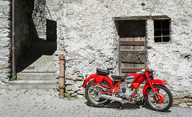 Fototapeta na wymiar Red Motorcycle on a background of old stone walls and doors. Old