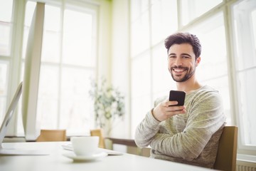 Smiling businessman holding mobile phone in office