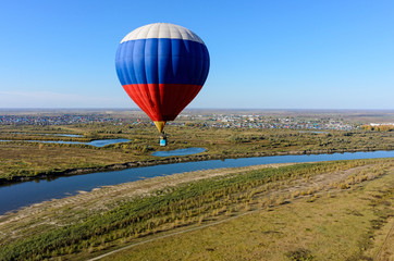 Kaskara, Russia - October 1, 2016: Hot air balloon flying over river landscape at autumn day. Kaskara at background. Tyumen region