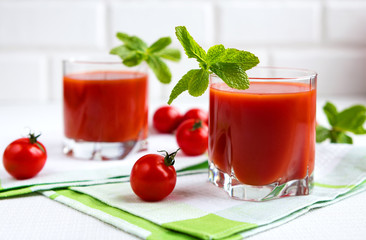 Tomato juice in a glass with a cherry and mint on a light background