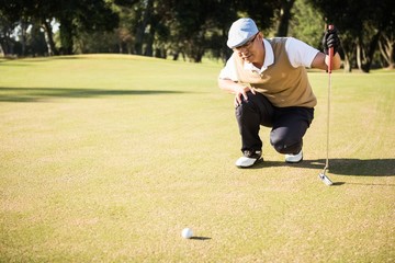 Side view of golfer crouching and looking his ball