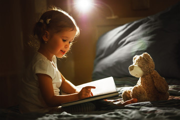 child girl reading a book in bed
