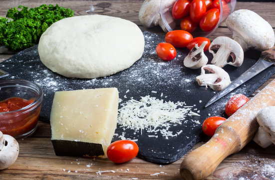 Pizza dough with ingredients on wood
