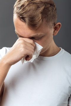Portrait of man having flu. Man blowing nose standing on gray background and