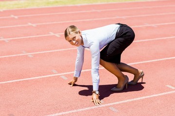 Fototapeta premium Portrait of businesswoman ready to run on running track