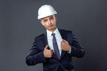 Handsome businessman in a helmet standing on gray background and straightens his jacket