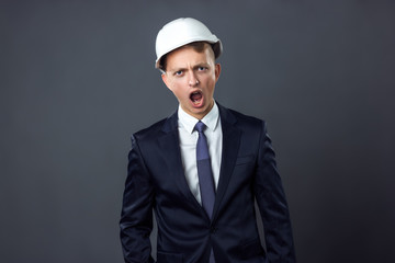 Handsome young engineer in a helmet he is screaming standing on gray background