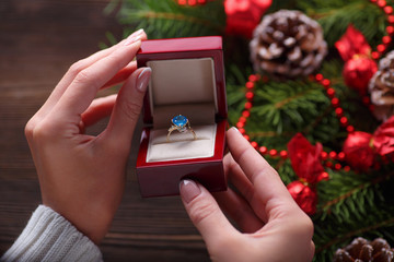 Engagement ring in female hands among Christmas decorations on wood background