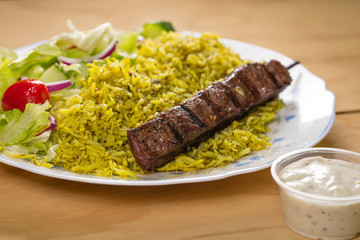 A grilled beef souvlaki skewers with tzatziki yogurt sauce, green rice, and fresh salad