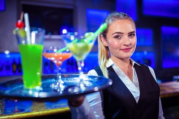 Portrait of pretty bartender holding serving tray with cocktails