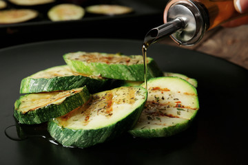 Female hand pouring oil over squash slices