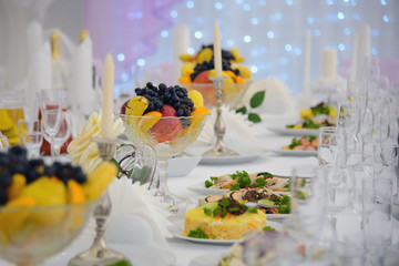 Table served dishes and candles. A festive reception at the table with food. Luxury table for a holiday celebration. Snacks and fruits on the occasion.