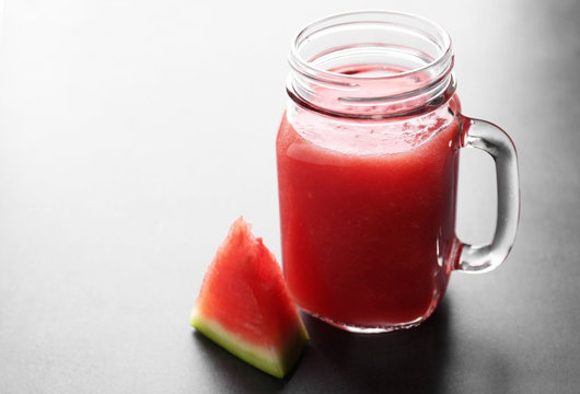 Jug with smoothie and watermelon slice on grey table