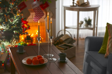 Wooden table with candles, cups and oranges in living room decorated for Christmas