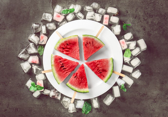Watermelon slices on sticks with ice cubes on table