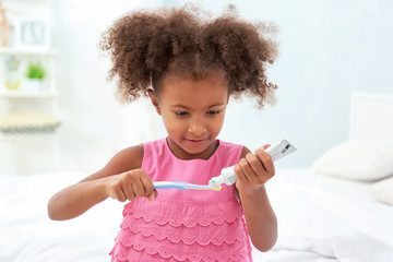 Cute African American girl brushing teeth in bathroom