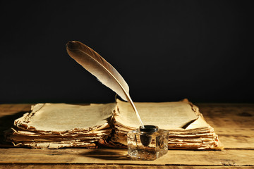 Feather pen with inkwell and stack of papers on dark background - obrazy, fototapety, plakaty