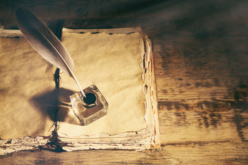 Feather pen with inkwell and stack of papers on wooden table closeup