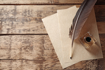 Feather pen with inkwell and blank papers on wooden background