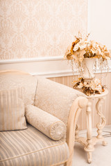 White classical sofa close-up and vase with golden branches and leaves on the litlle table. Horizontal