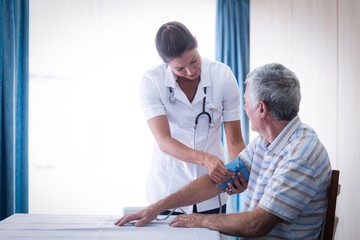 Female doctor checking blood pressure of senior man