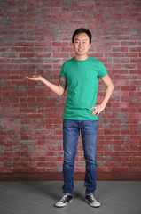 Obraz na płótnie Canvas Asian man in blank green t-shirt standing against brick wall