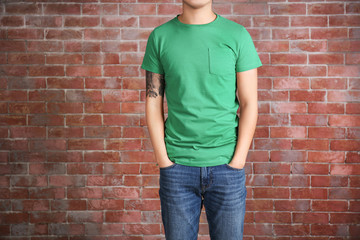 Young man in blank green t-shirt standing against brick wall, close up